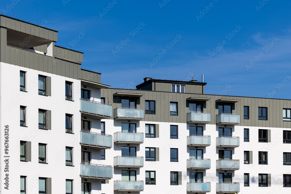 White and beige facade of a newly built apartment block. Clear blue sky above the building. Photo taken on a sunny day