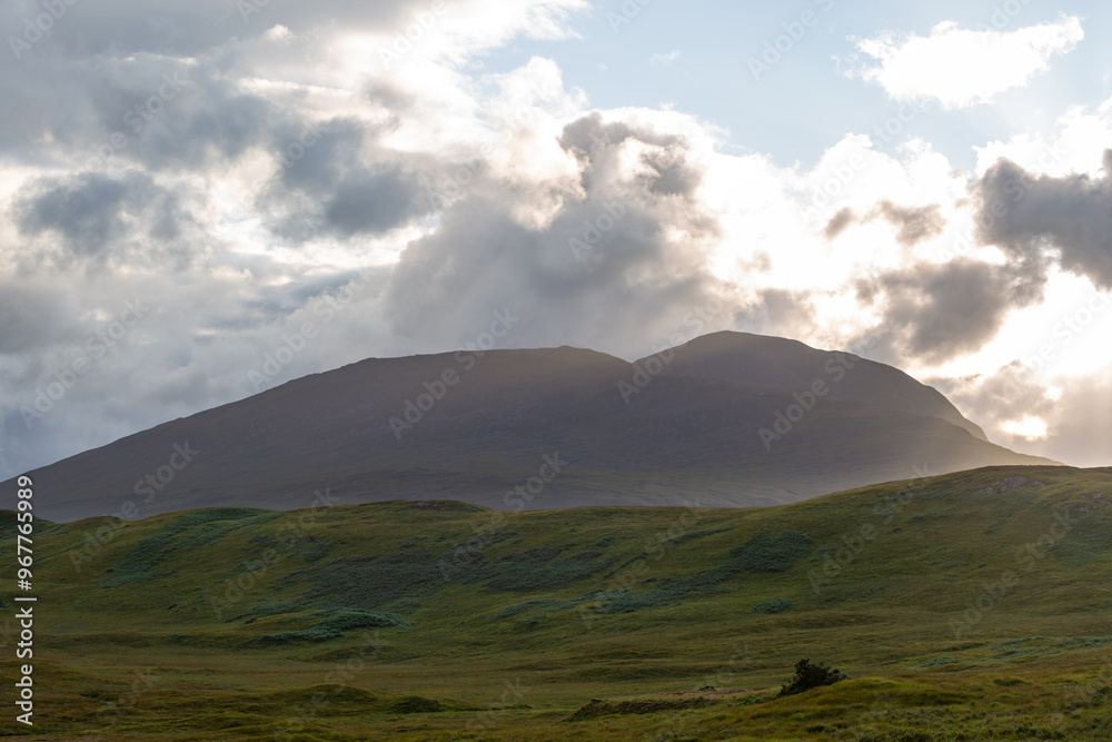 Obraz premium Scottish highlands at sunset, Image shows a mountain range near Glencoe as the sun sets while shining through clouds