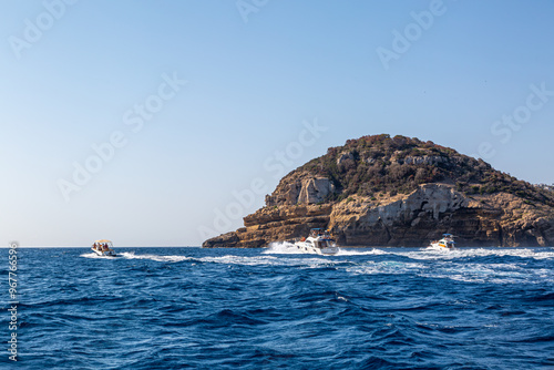 Three boats travelling side by side in the Mediterranean following the coastline 