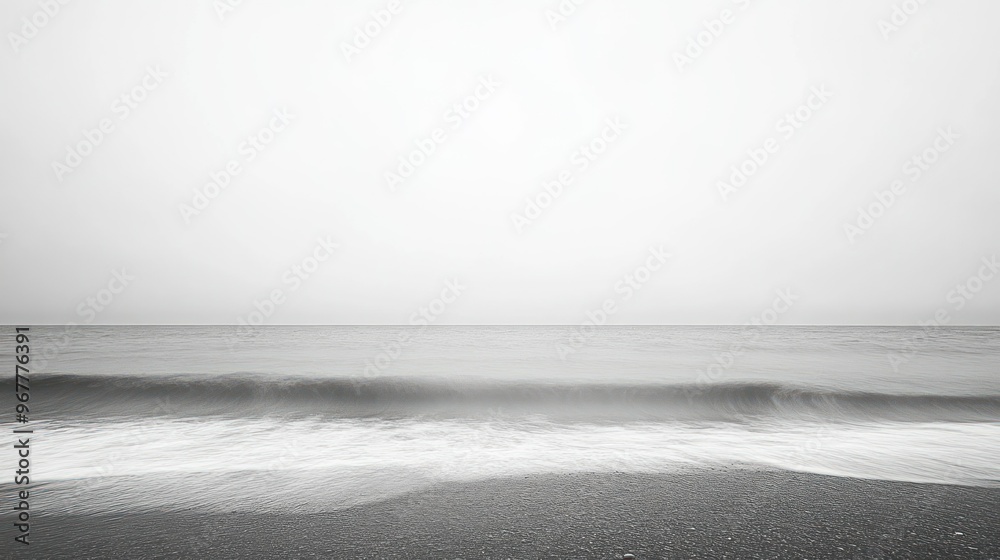 A serene black-and-white seascape with gentle waves and a foggy horizon.