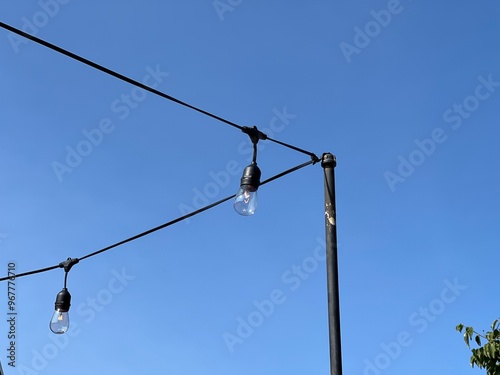 Outdoor hanging string of patio lights against a blue sky with copy space