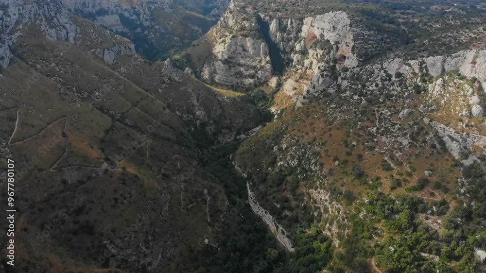 Aerial view of a breathtaking canyon surrounded by majestic mountains and a serene valley, Cavagrande del Cassibile, Italy. Aerial view of a breathtaking canyon surrounded by majestic mountains and a serene valley, Cavagrande del Cassibile, Italy.