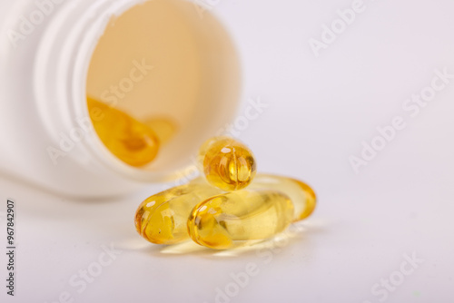 White plastic bottle spilling yellow medicinal capsules on a white surface