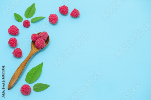 Wooden spoon of ripe raspberries on table, angle view. Three raspberries in one spoon and leaves on a blue wooden table