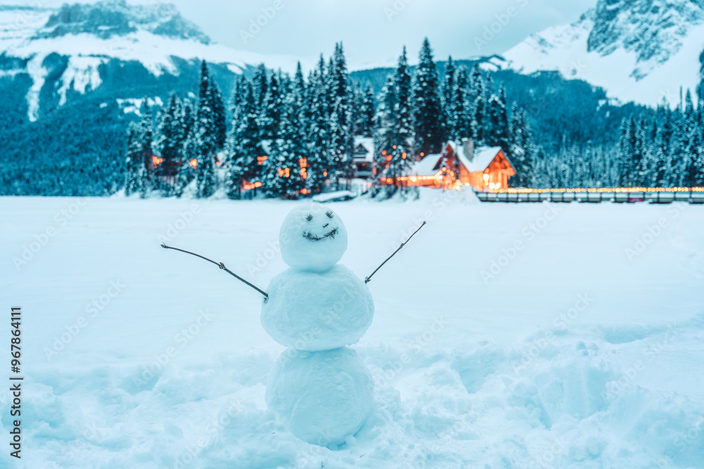 Fototapeta premium Frozen Emerald Lake with snowman and wooden lodge glowing in pine forest at Yoho national park, Canada