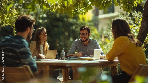 Group of friends collaborating on a project outdoors under lush green trees during a sunny afternoon