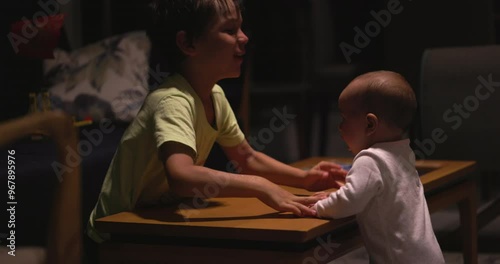 Brother plays with infant baby girl in living room at night