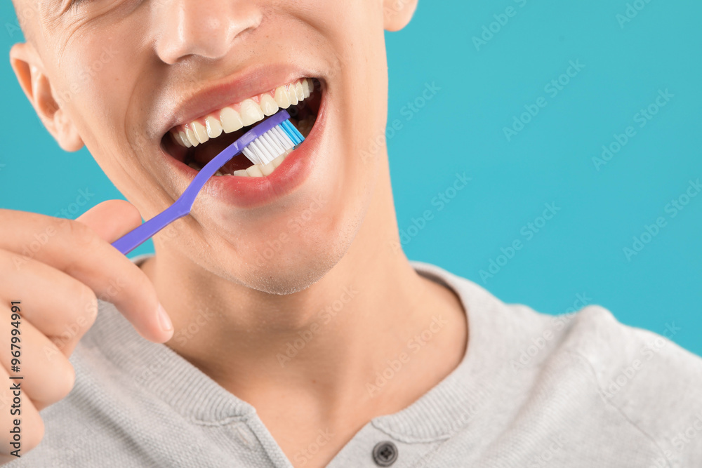 Young man brushing his teeth on light blue background, closeup Young man brushing his teeth on light blue background, closeup