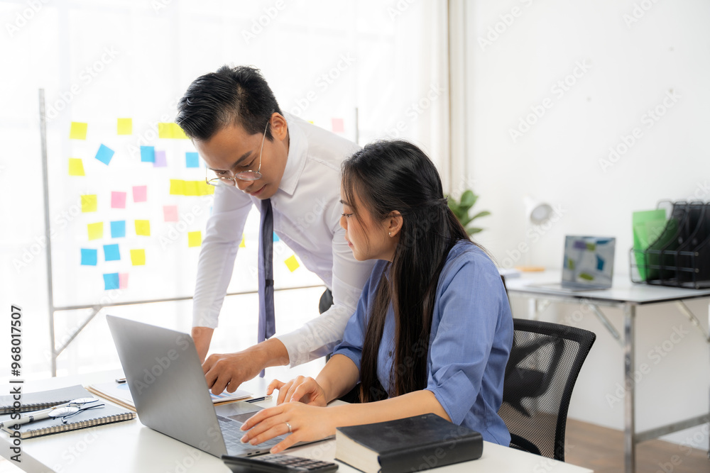 Focused Collaboration: Male mentor guides female colleague through project details on a laptop, fostering a productive learning environment in a modern office. Focused Collaboration: Male mentor guides female colleague through project details on a laptop, fostering a productive learning environment in a modern office.