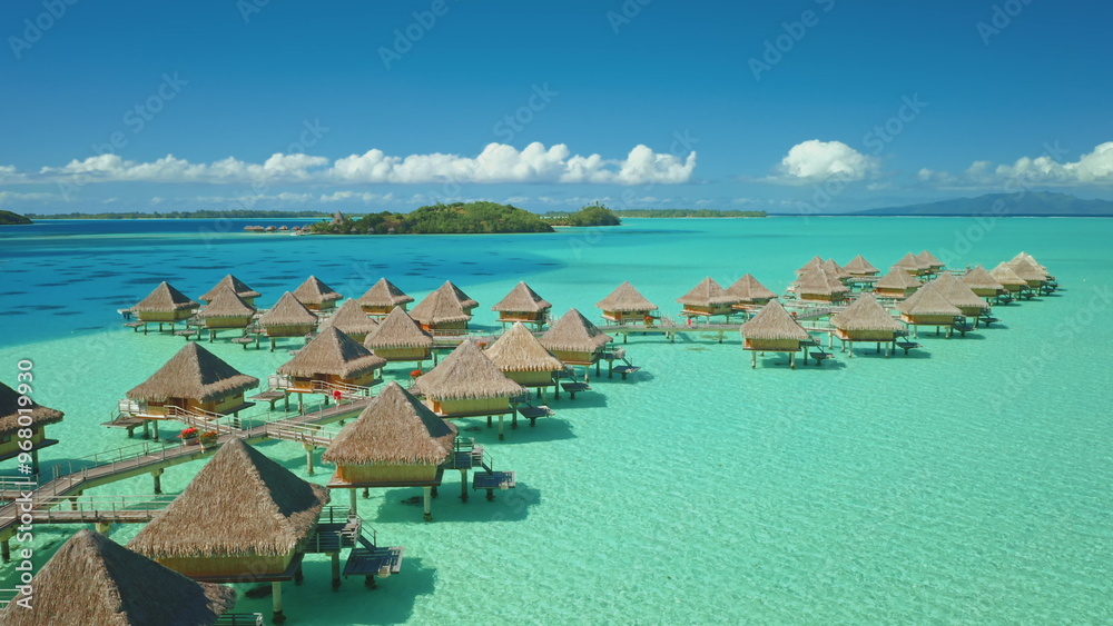 Fototapeta premium Luxury overwater bungalows in turquoise lagoon of Bora Bora tropical island. Eco tourism wooden huts under blue sky. Popular tourist destination. Remote wild nature paradise, exotic summer travel