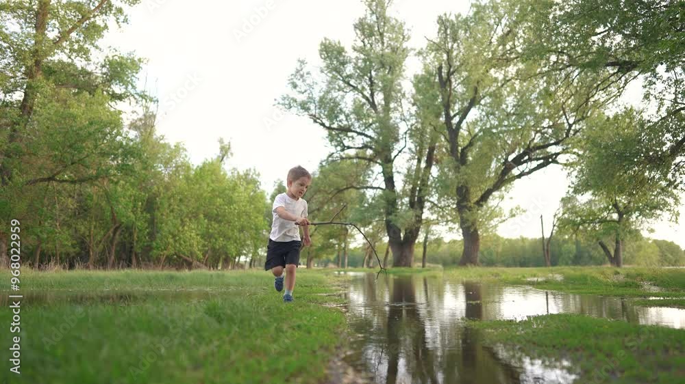 little boy playing on the nature. nature people and parks concept. a boy in a white T-shirt happily plays with clean water in a big lifestyle puddle in a large green park little boy playing on the nature. nature people and parks concept. a boy in a white T-shirt happily plays with clean water in a big lifestyle puddle in a large green park