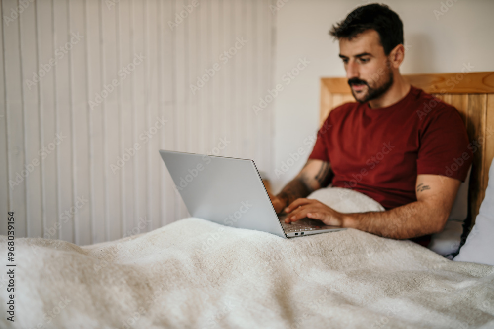 Focused man working on a laptop from the bed