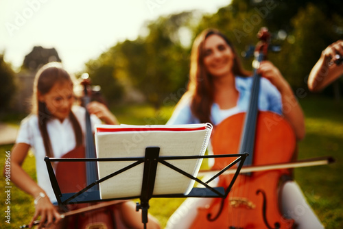 People, instruments and book in nature for music, talent and entertainment for event. Musicians, string trio and smile on grass for art, rehearsal and practice for creativity with skill development photo