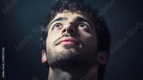 A close-up of a man looking up with a slight smile, his face illuminated softly, emphasizing his features against a plain backdrop photo