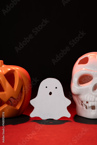 fantasma lindo hecho de papel, junto a calabaza y cráneo de plástico iluminados por una luz roja con espacio para texto photo