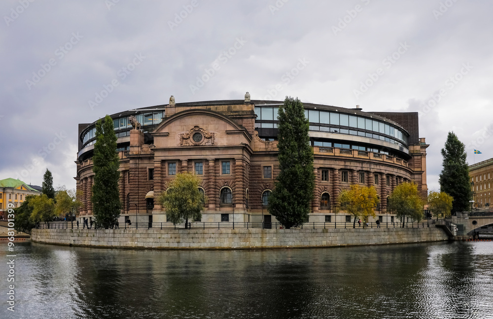 A stunning blend of historic and contemporary architecture features the Parliament building of Sweden in Stockholm, surrounded by trees as overcast skies create a dramatic backdrop for the scene. A stunning blend of historic and contemporary architecture features the Parliament building of Sweden in Stockholm, surrounded by trees as overcast skies create a dramatic backdrop for the scene.