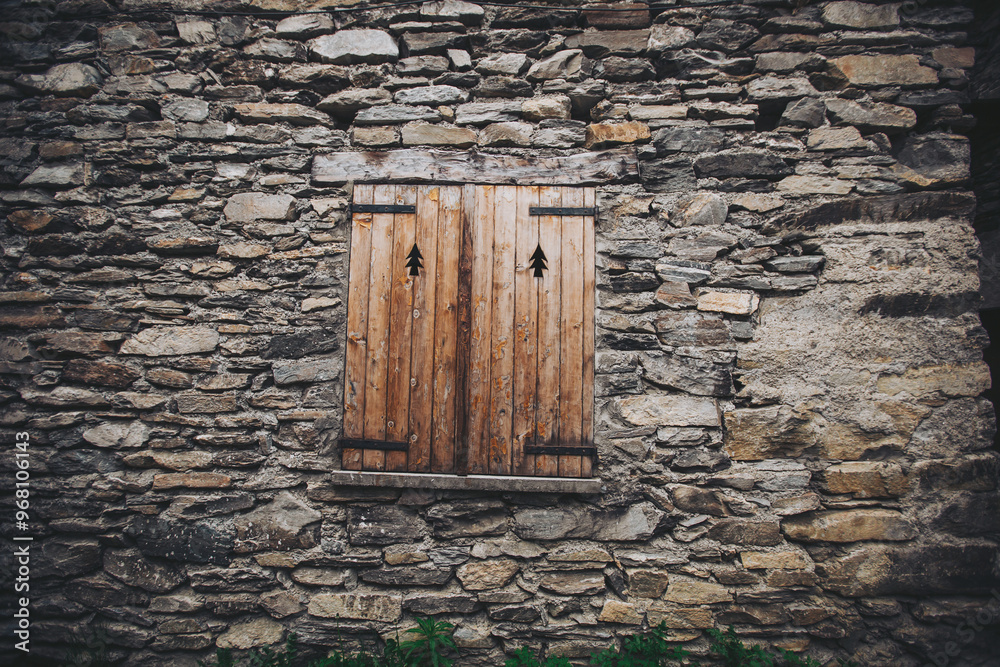 antique wooden window on a construction made of slate, typical of the villages of architecture in the province of Alps Mountains. Closed wooden window shutters with with typical alpine decoration antique wooden window on a construction made of slate, typical of the villages of architecture in the province of Alps Mountains. Closed wooden window shutters with with typical alpine decoration