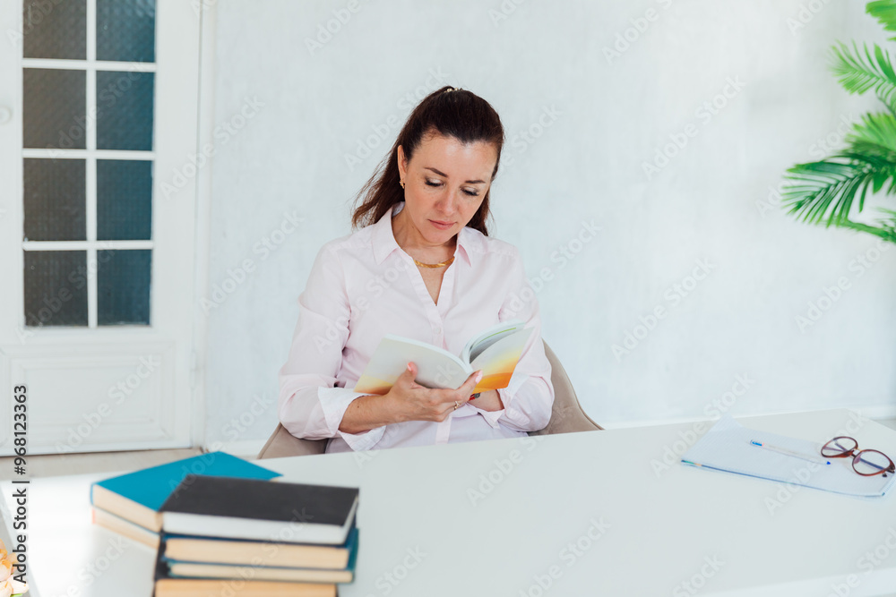 Beautiful business woman reading a book at her desk in the office Beautiful business woman reading a book at her desk in the office