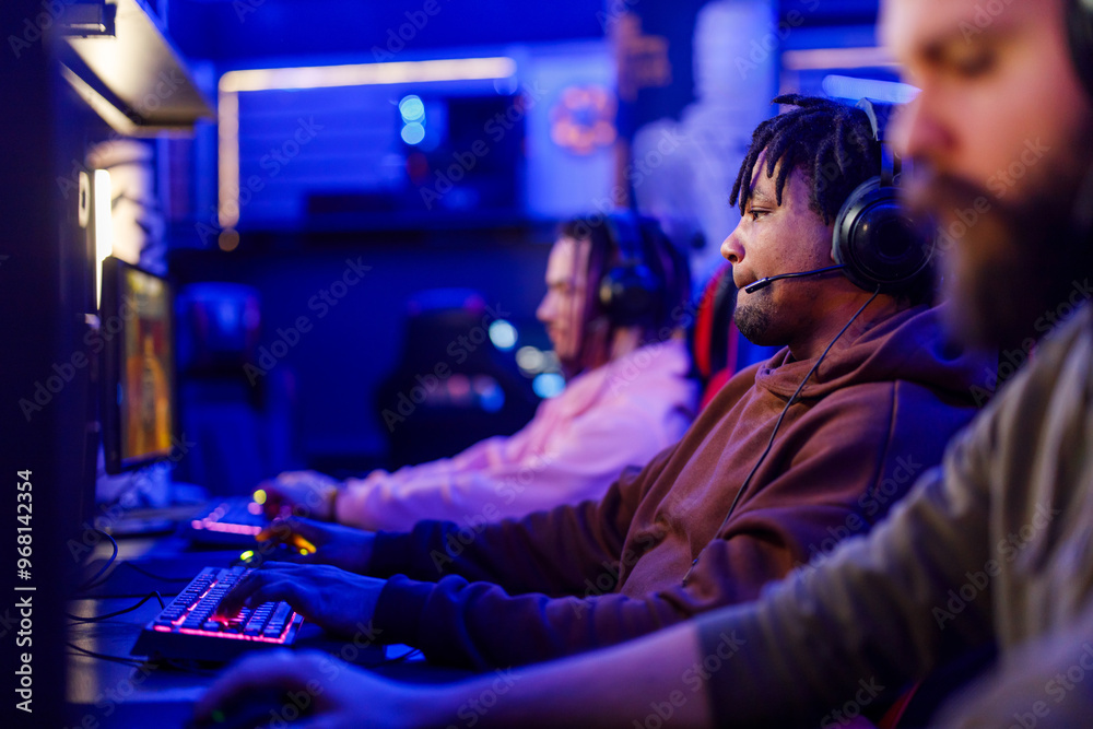 Side view of interracial gamer with headset playing mmo fps in cybercafe Side view of interracial gamer with headset playing mmo fps in cybercafe