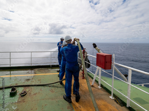 Seamen during fire emergency training drill, on board a merchant cargo ship, wearing fire fighting equipment and helmets. Rigged fire hose for jet spray, with emergency fire pump. photo