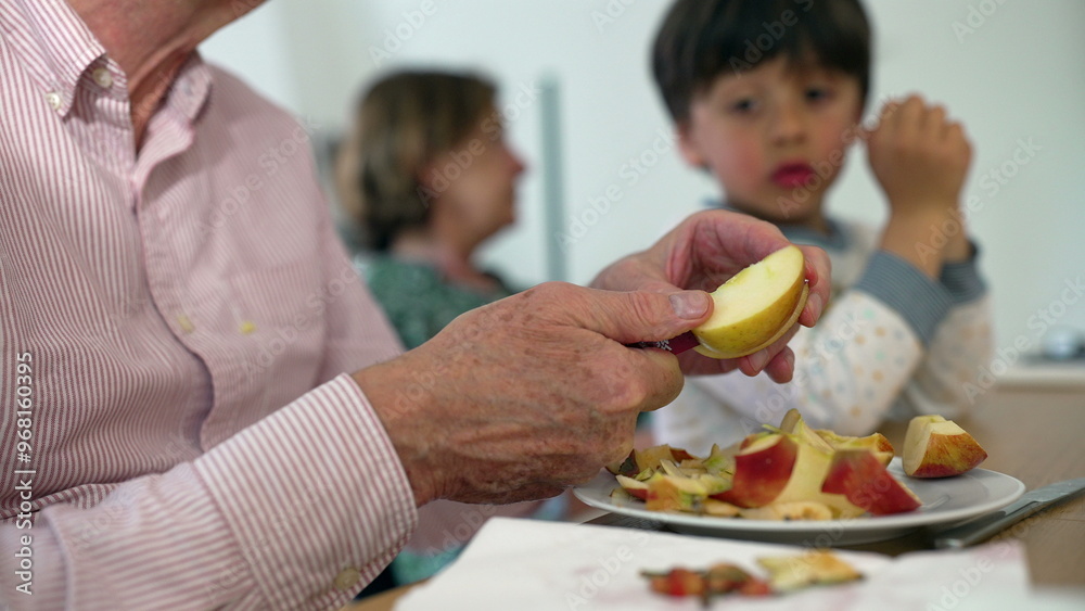 Senior man slicing an apple with a knife, young child watching in the background, indoor family setting, highlighting generational connection and simple daily tasks Senior man slicing an apple with a knife, young child watching in the background, indoor family setting, highlighting generational connection and simple daily tasks