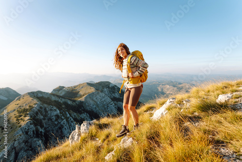 A joyful hiker enjoys the breathtaking view from a mountain summit during a sunny afternoon in the serene foothills. Nature, active life, travel.