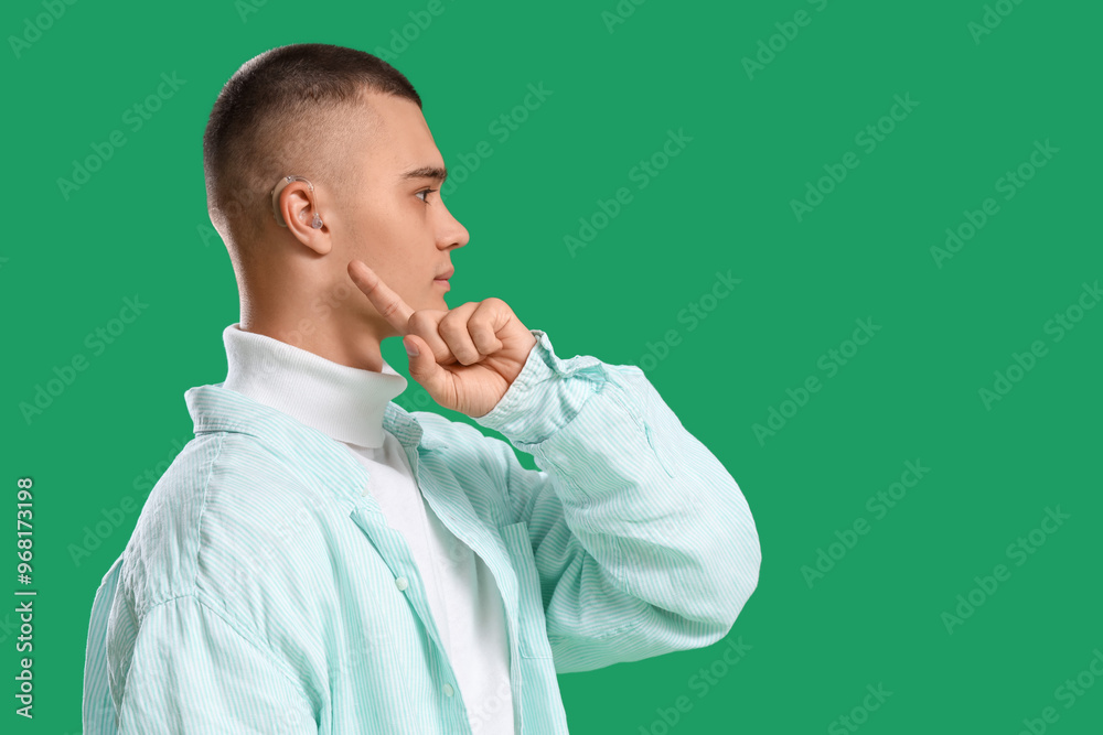 Teenage boy pointing at hearing aid on green background