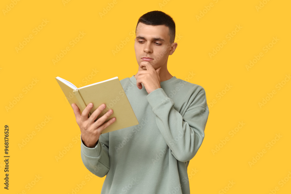 Thoughtful young man reading book on yellow background Thoughtful young man reading book on yellow background
