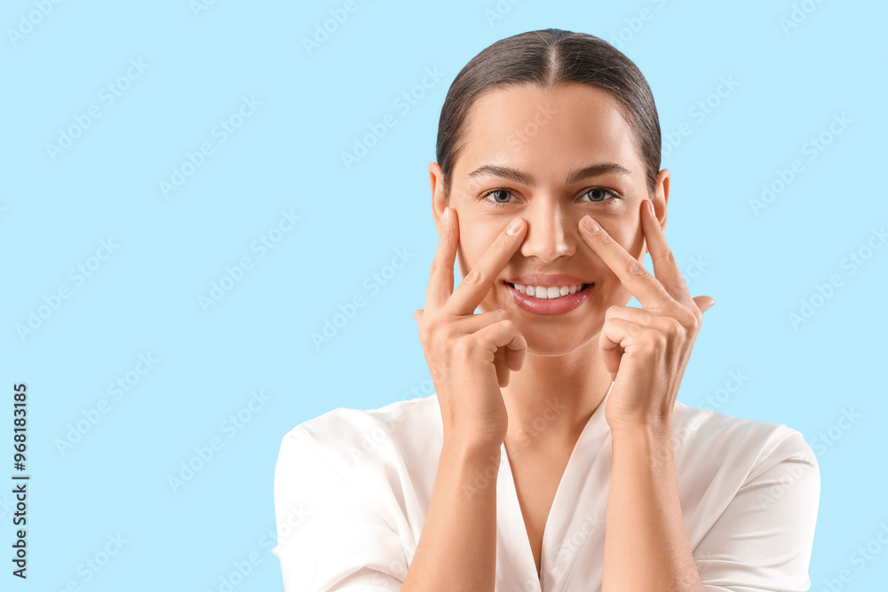 Beautiful young woman massaging her face on blue background, closeup Beautiful young woman massaging her face on blue background, closeup