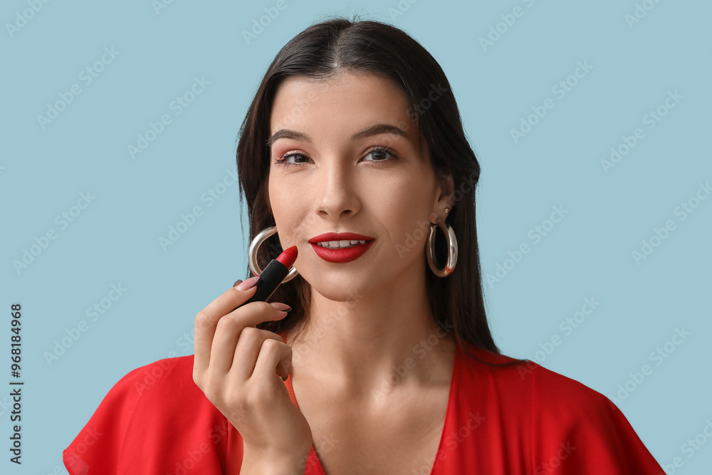 Beautiful young woman applying red lipstick on blue background Beautiful young woman applying red lipstick on blue background