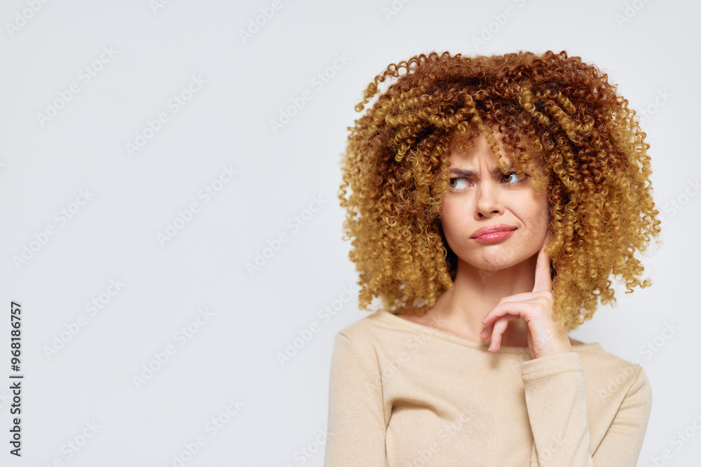 Woman with curly hair, making a thoughtful expression against a light gray background, wearing a beige sweater Her confused look conveys curiosity and contemplation Woman with curly hair, making a thoughtful expression against a light gray background, wearing a beige sweater Her confused look conveys curiosity and contemplation