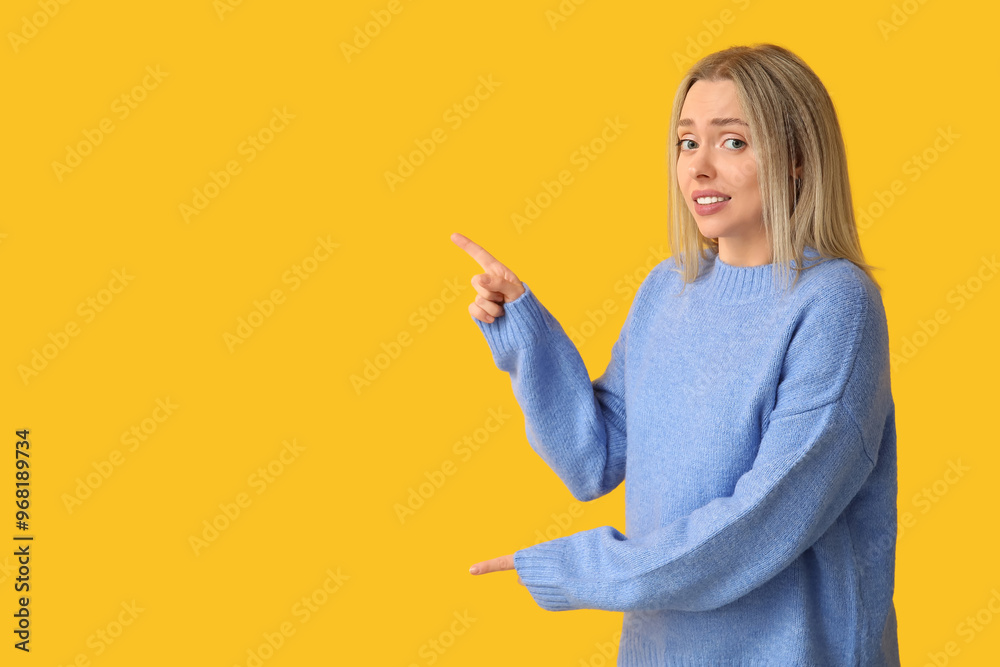 Young woman feeling awkward while pointing at something on yellow background Young woman feeling awkward while pointing at something on yellow background
