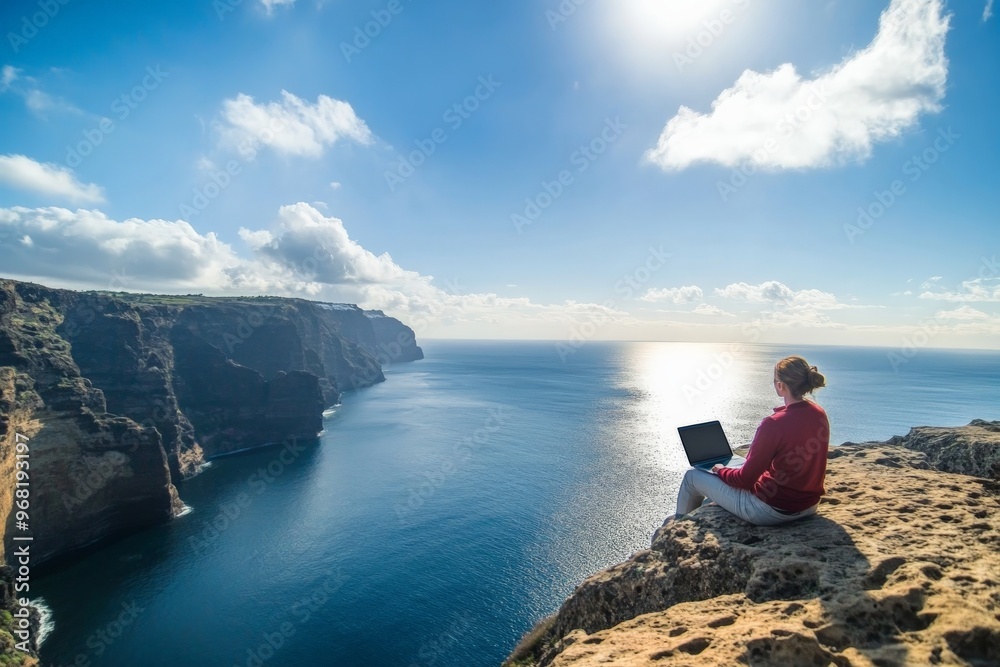 A person sits with a laptop at the edge of a cliff overlooking a vast ocean, under a clear blue sky. The scene exudes solitude, freedom, and connection with nature and technology. A person sits with a laptop at the edge of a cliff overlooking a vast ocean, under a clear blue sky. The scene exudes solitude, freedom, and connection with nature and technology.