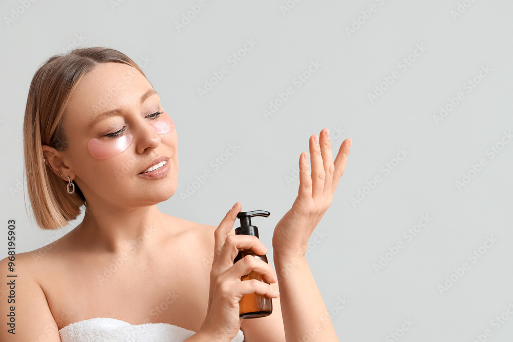 Beautiful mature woman with under-eye patches applying cosmetic product on her hand against grey background Beautiful mature woman with under-eye patches applying cosmetic product on her hand against grey background