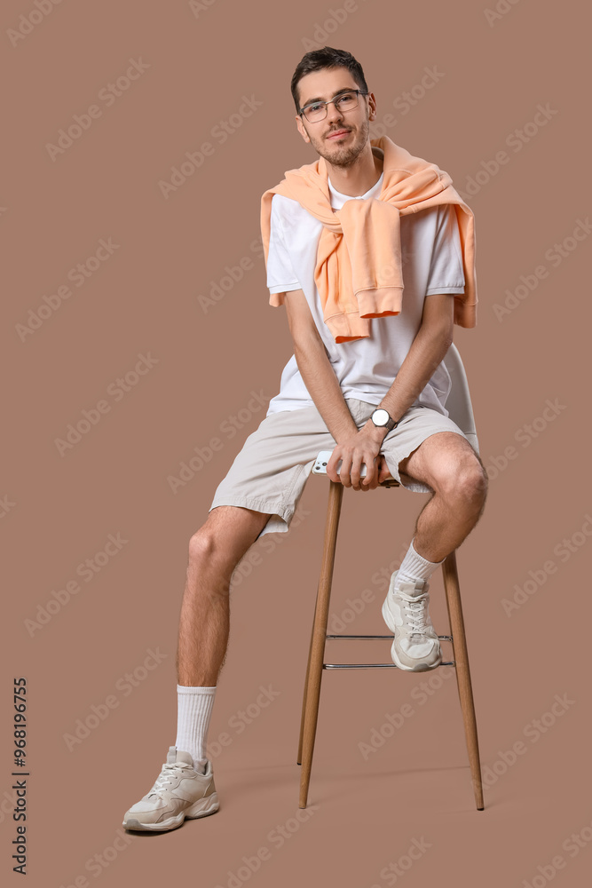 Handsome young man in stylish clothes with eyeglasses sitting on chair and posing against beige background Handsome young man in stylish clothes with eyeglasses sitting on chair and posing against beige background
