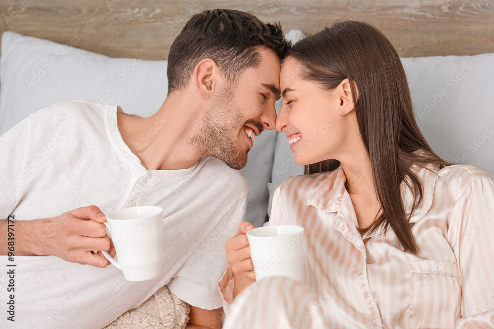 Young couple with cups of coffee lying on bed Young couple with cups of coffee lying on bed
