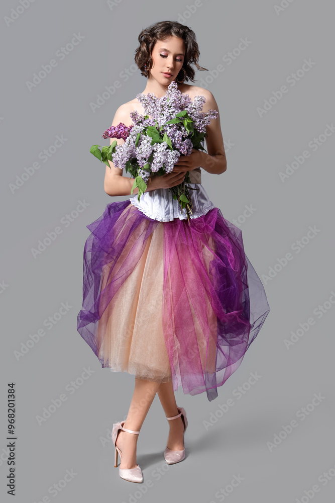 Naklejka premium Beautiful young woman with bouquet of blooming lilac flowers on grey background