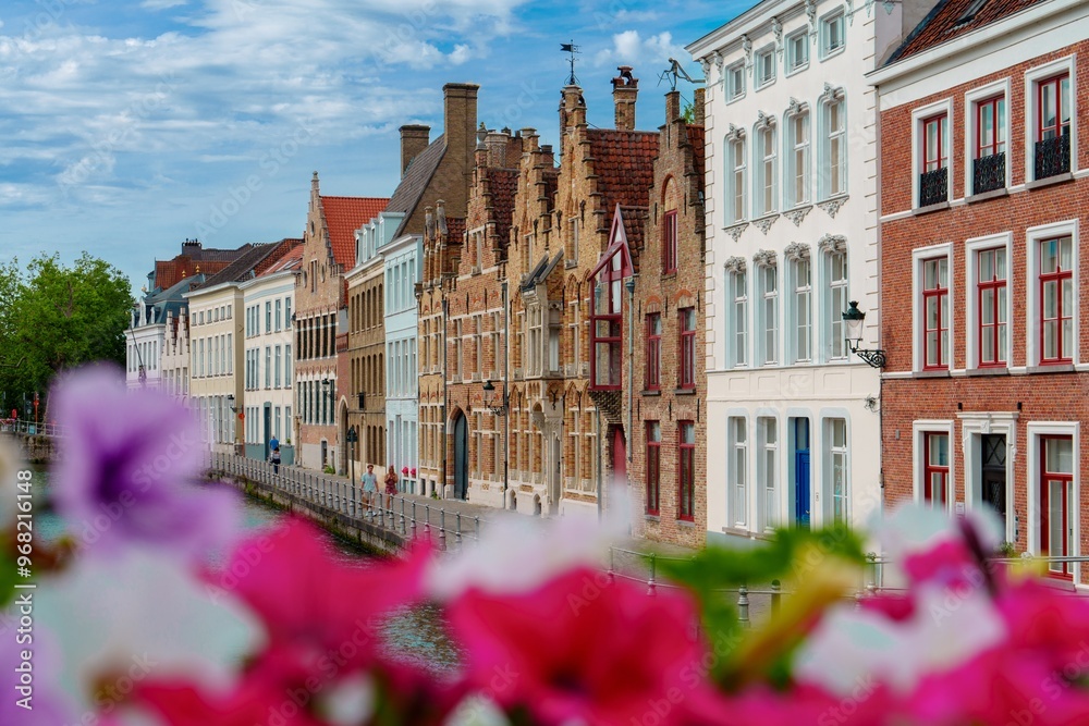Obraz premium Bruges, Belgium, A stunning canal scene in a quaint European city, featuring colorful flowers lining the banks and beautifully preserved traditional houses. Ideal for leisurely strolls, photography