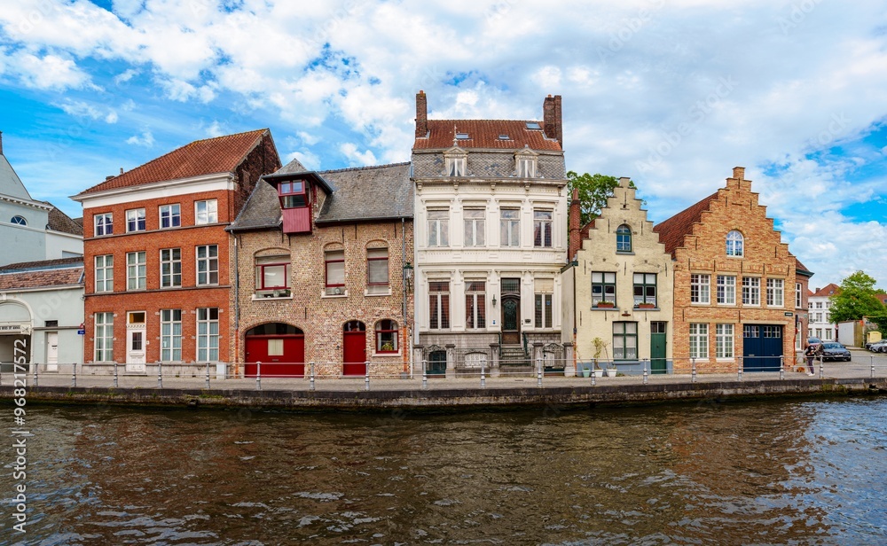 This image features a picturesque canal in Bruges, Belgium. The canal is surrounded by colorful houses and a blue sky with white clouds. The image is perfect for a travel brochure or website. This image features a picturesque canal in Bruges, Belgium. The canal is surrounded by colorful houses and a blue sky with white clouds. The image is perfect for a travel brochure or website.