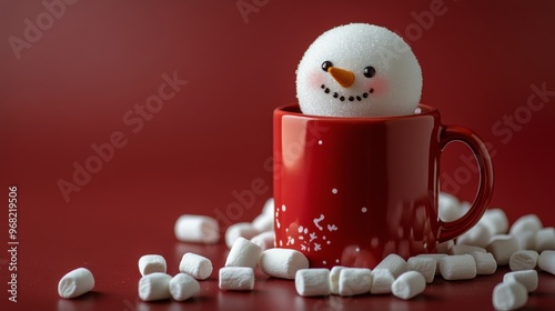Cheerful snowman decoration in a red mug surrounded by marshmallows on a fest...