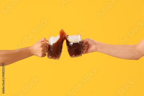 Male hands with glasses of cold beer clinking on yellow background. Octoberfest celebration photo