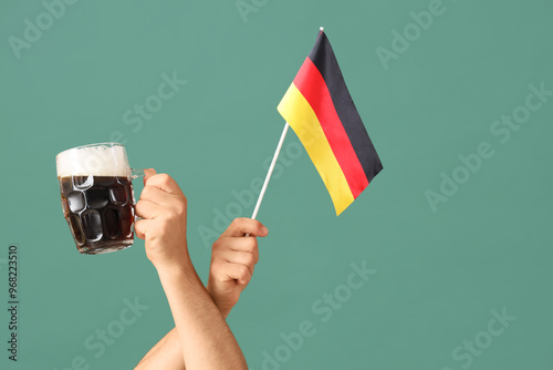 Male hands with mug of cold beer and Germany flag on green background. Octoberfest celebration photo