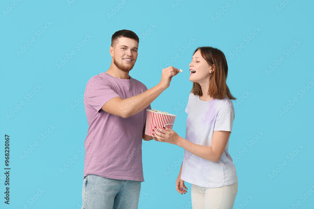 Happy young couple with bucket of popcorn on blue background Happy young couple with bucket of popcorn on blue background