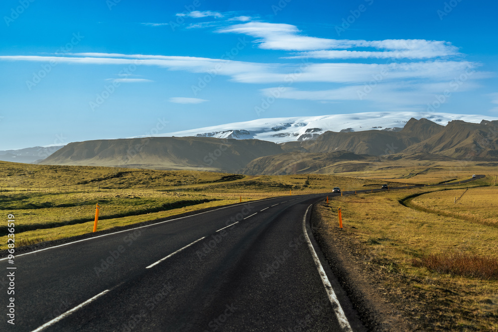 A winding road stretches towards towering mountains and glaciers in Iceland, with a dramatic sky overhead A winding road stretches towards towering mountains and glaciers in Iceland, with a dramatic sky overhead