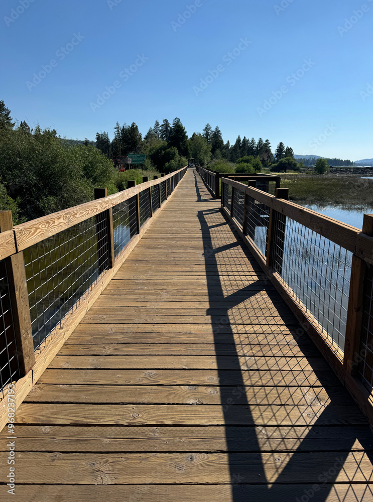 Fototapeta premium wooden boardwalk over a lake, forest and mountains in the background - Big Bear Lake, California