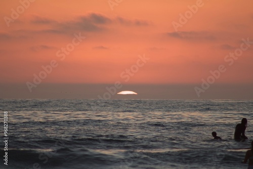 Surfer silhouettes sitting on surfboards in ocean waves watching orange pink sunset in Pacific Beach, San Diego photo