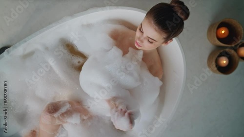 Peaceful lady relaxing bubbles bath touching gentle skin top view. Woman lying