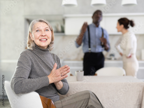 Elderly woman smiling during family quarrel between couple of adult man and woman in kitchen
