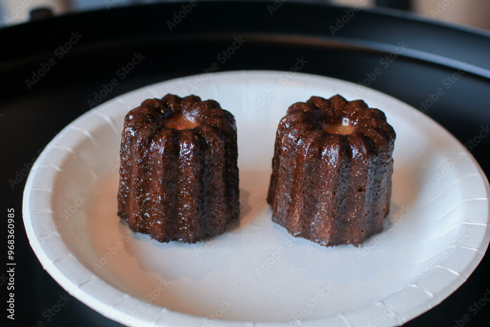 Hand pick up Homemade Canelés de Bordeaux pastry with rum and vanilla in white plate. Caramelized crust specialty. Traditional French sweet dessert Hand pick up Homemade Canelés de Bordeaux pastry with rum and vanilla in white plate. Caramelized crust specialty. Traditional French sweet dessert