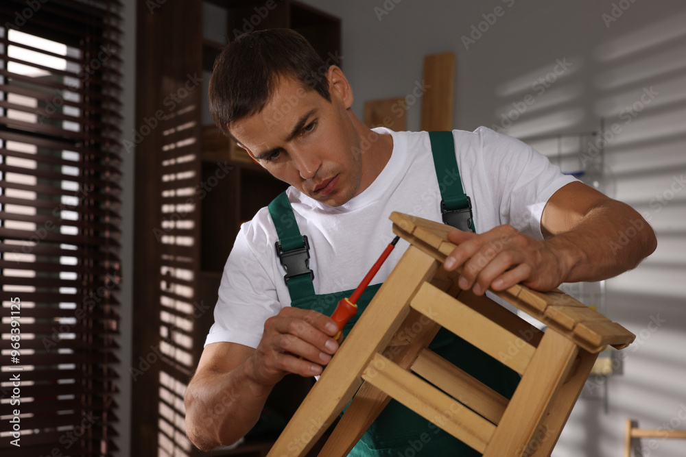 Obraz premium Man repairing wooden stool with screwdriver indoors